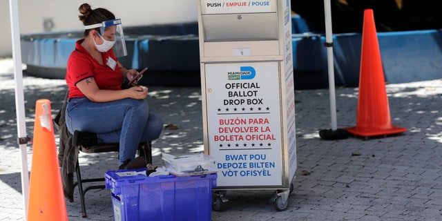 A poll worker wears personal protective equipment as she watches a ballot box for mailed ballots outside a polling station during advance voting on August 7, 2020, in Miami Beach, California. Florida (AP Photo / Lynne Sladky)