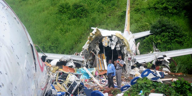 Officials stand on the debris of the Air India Express flight that skidded off a runway while landing at the airport in Kozhikode, Kerala state, India, Saturday, Aug. 8, 2020. (Associated Press)