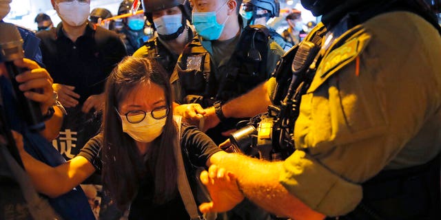 Pro-democracy protesters, front left and rear left, are surrounded by riot police during a news conference to mark one-year anniversary of the Yuen Long subway attack at the subway station in Hong Kong, Tuesday, July 21, 2020. A gang of men in white shirts brutally beat dozens of people inside the train station on July 21 last year. (AP Photo/Kin Cheung)