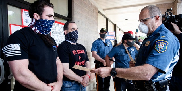 A police officer issues Atilis Gym co-owners Ian Smith, left, and Frank Trumbetti, center, summons outside their gym in Bellmawr, N.J., Tuesday, May 19, 2020. After repeatedly defying the governor's order to remain closed during the COVID-19 pandemic Smith and Trumbetti had been arrested on contempt charges. (AP Photo/Matt Rourke, File)