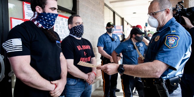 A police officer issues Atilis Gym co-owners Ian Smith and Frank Trumbetti summons outside their gym in Bellmawr, N.J., Tuesday, May 19, 2020. (AP Photo/Matt Rourke, File)