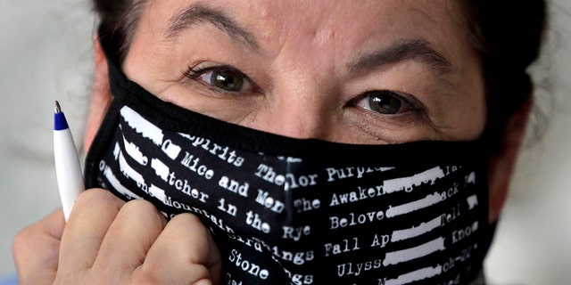 Poet Tammi Truax poses at her writing table, wearing a protective mask due to the COVID-19 virus outbreak, Wednesday, July 29, 2020, at her home in Eliot, Maine. Truax, the poet laureate for Portsmouth, N.H., pens a weekly pandemic poem that is included in the city's COVID-19 newsletter. (AP Photo/Charles Krupa)
