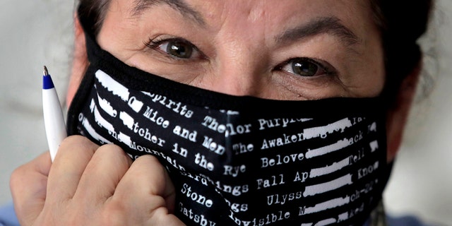 Poet Tammi Truax poses at her writing table, wearing a protective mask due to the COVID-19 virus outbreak, Wednesday, July 29, 2020, at her home in Eliot, Maine. Truax, the poet laureate for Portsmouth, N.H., pens a weekly pandemic poem that is included in the city's COVID-19 newsletter. (AP Photo/Charles Krupa)