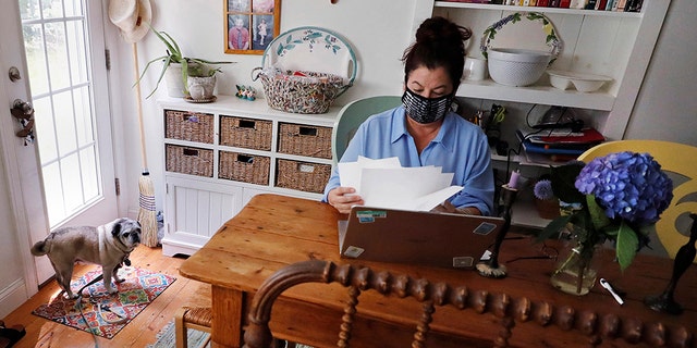 Poet Tammi Truax looks over her recent work, as her pug "Pie" looks on, while seated at her writing table, wearing a protective mask due to the COVID-19 virus outbreak, Wednesday, July 29, 2020, at her home in Eliot, Maine. Truax, the poet laureate for Portsmouth, N.H., pens a weekly pandemic poem that is included in the city's COVID-19 newsletter. (AP Photo/Charles Krupa)
