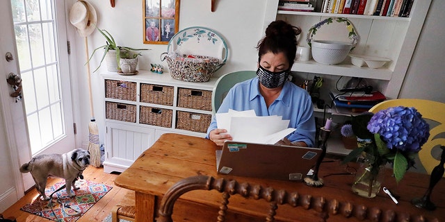 Poet Tammi Truax looks over her recent work, as her pug "Pie" looks on, while seated at her writing table, wearing a protective mask due to the COVID-19 virus outbreak, Wednesday, July 29, 2020, at her home in Eliot, Maine. Truax, the poet laureate for Portsmouth, N.H., pens a weekly pandemic poem that is included in the city's COVID-19 newsletter. (AP Photo/Charles Krupa)