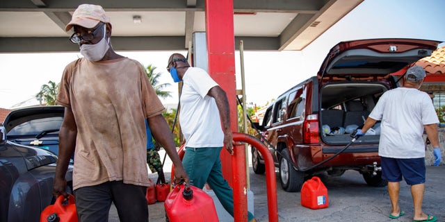A resident walks with containers filled with gasoline at Cooper's gas station before the arrival of Hurricane Isaias in Freeport, Grand Bahama, Bahamas, Friday, July 31, 2020. (AP Photo/Tim Aylen)