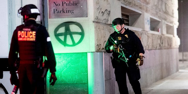 Department of Homeland Security officers guard a back entrance to the Mark O. Hatfield U.S. Courthouse on Saturday, Aug. 1, 2020, in Portland, Ore.  (AP Photo/Noah Berger)