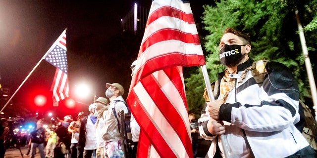 Navy veteran Adam Winther holds a flag while forming a "Wall of Vets" during a Black Lives Matter protest at the Mark O. Hatfield United States Courthouse on Friday, July 31, 2020, in Portland, Ore. Following an agreement between Democratic Gov. Kate Brown and the Trump administration to reduce federal officers in the city, nightly protests remained largely peaceful without major confrontations between demonstrators and officers. (AP Photo/Noah Berger)