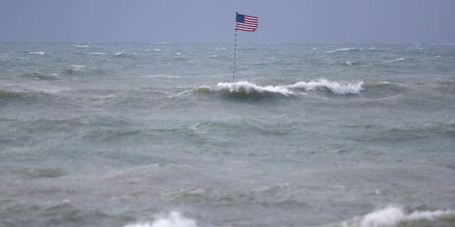 An American flag flies from the shipwreck of the Breconshire, as waves churned up by Tropical Storm Isaias crash around it, Sunday, Aug. 2, 2020, in Vero Beach, Fla.