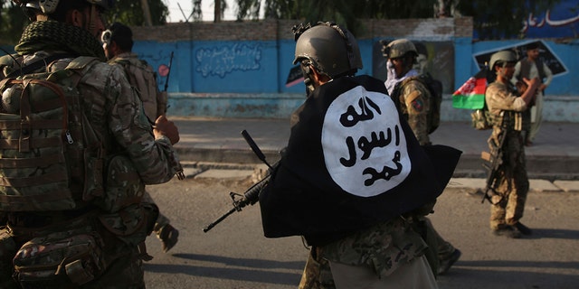 An Afghan security personnel covers himself with the Islamic State group's flag after an attack in the city of Jalalabad, east of Kabul, Afghanistan, Monday, Aug. 3, 2020. (AP Photo/Rahmat Gul)