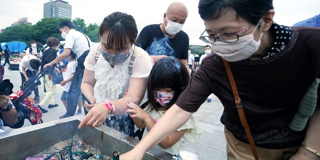 People burn joss sticks in front of the cenotaph for the atomic bombing victims before the start of a ceremony to mark the 75th anniversary of the U.S. bombing in Hiroshima, western Japan, early Thursday, Aug. 6, 2020. (AP Photo/Eugene Hoshiko)