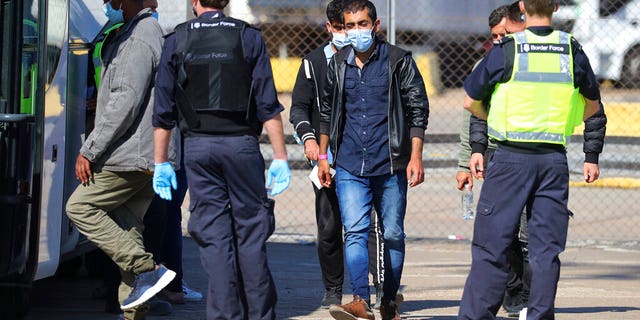 Border Force officers escort a group of men thought to be migrants to a waiting bus, after they were brought into the port city of Dover, England, from small boats, Aug. 7. There have been a number of small boat incidents over recent days, with some unseaworthy vessels trying to make the journey from France across The Channel, one of the busiest shipping lanes in the world. (Gareth Fuller/PA via AP)