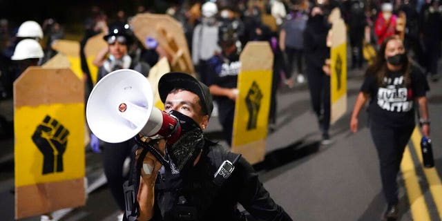 A protester leads a crowd of demonstrators toward the Multnomah County Sheriff's Office on Saturday, Aug. 7, 2020 in Portland, Ore. (AP Photo/Nathan Howard)