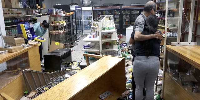 Yogi Dalal hugs his daughter Jigisha as his other daughter Kajal, left, bows her head at the family food and liquor store Monday, Aug. 10, 2020, after the family business was vandalized in Chicago. (AP Photo/Charles Rex Arbogast)