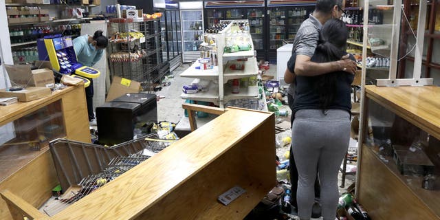 Yogi Dalal hugs his daughter Jigisha as his other daughter Kajal, left, bows her head at the family food and liquor store Monday, Aug. 10, 2020, after the family business was vandalized in Chicago. (AP Photo/Charles Rex Arbogast)