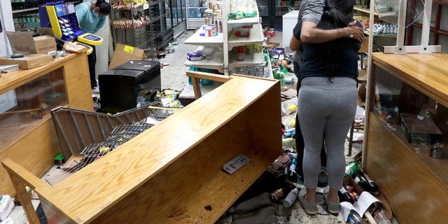 Yogi Dalal hugs his daughter Jigisha as his other daughter Kajal, left, bows her head at the family food and liquor store Monday, Aug. 10, 2020, after the family business was vandalized in Chicago. (AP Photo/Charles Rex Arbogast)