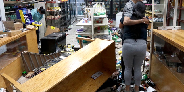 Yogi Dalal hugs his daughter Jigisha as his other daughter Kajal, left, bows her head at the family food and liquor store Monday, Aug. 10, 2020, after the family business was vandalized in Chicago. (AP Photo/Charles Rex Arbogast)