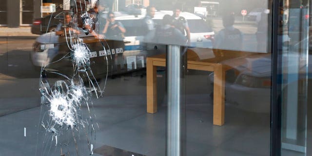 Chicago police officers are reflected in a broken window as they gather, Monday, Aug. 10, 2020, outside an Apple Store that was vandalized overnight in the Lincoln Park neighborhood in Chicago. 