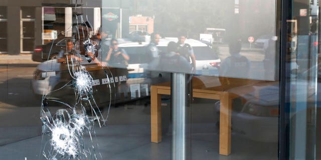 Chicago police officers are reflected in a broken window as they gather, Monday, Aug. 10, 2020, outside an Apple Store that was vandalized overnight in the Lincoln Park neighborhood in Chicago. 