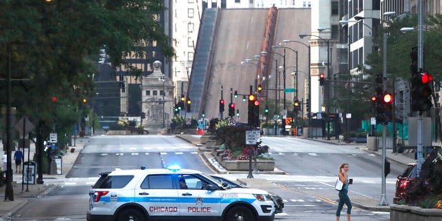 A pedestrian walks across Michigan Ave., Monday, Aug. 10, 2020, past a Chicago police department vehicle, a few blocks north of the raised Michigan Ave. bridge over the Chicago river after overnight vandalism in Chicago. 