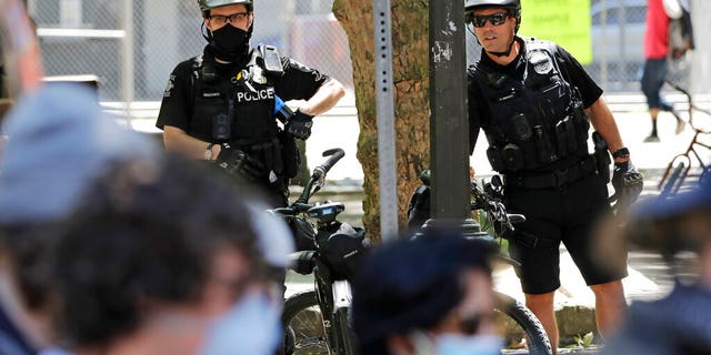 FILE - In this July 20, 2020, file photo, police officers look on at protesters in Seattle. (AP Photo/Elaine Thompson, File)