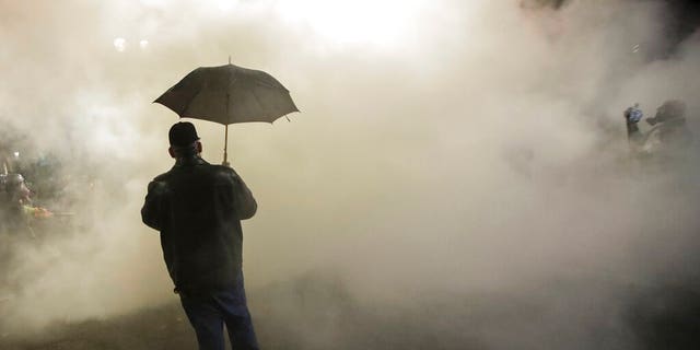 In this July 25, 2020, file photo, a protester carries an umbrella as federal officers deploy tear gas during a protest. (AP Photo/Marcio Jose Sanchez, File)