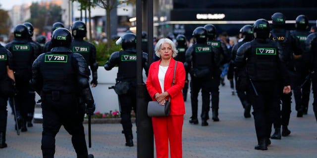 A woman stands in a street as police gather to block protesters during a mass protest following presidential elections in Minsk, Belarus, Monday, Aug. 10, 2020. 