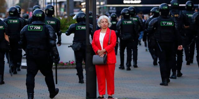 A woman stands in a street as police gather to block protesters during a mass protest following presidential elections in Minsk, Belarus, Monday, Aug. 10, 2020.