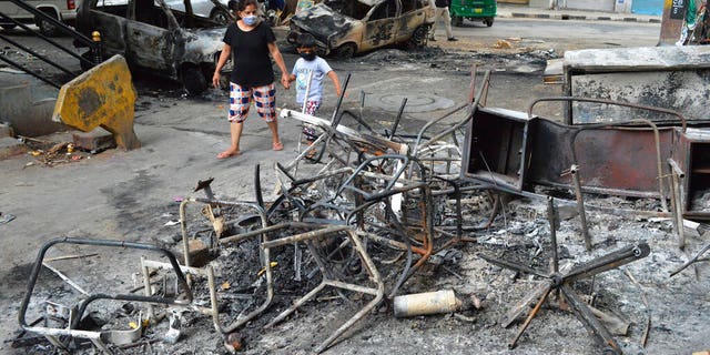 A woman and child walk past the wreckage of vehicles and furniture burnt during violent protests in Bengaluru, India, on Wednesday, Aug. 12, 2020. (AP Photo)
