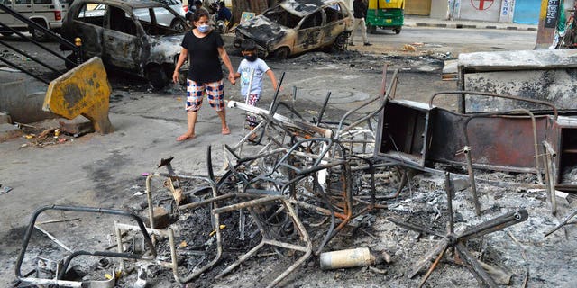 A woman and child walk past the wreckage of vehicles and furniture burnt during violent protests in Bengaluru, India, on Wednesday, Aug. 12, 2020. (AP Photo)