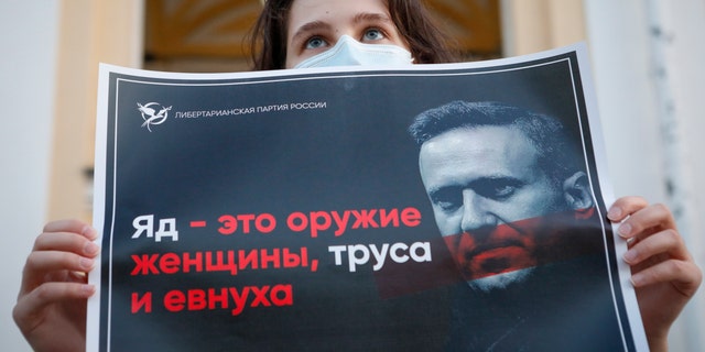 A protester stands holds a poster reads "poison is the weapon of a woman, a coward and a eunuch!" during a picket in support of Russian opposition leader Alexei Navalny in the center of St. Petersburg, Russia, Thursday, Aug. 20, 2020. (AP Photo/Elena Ignatyeva)