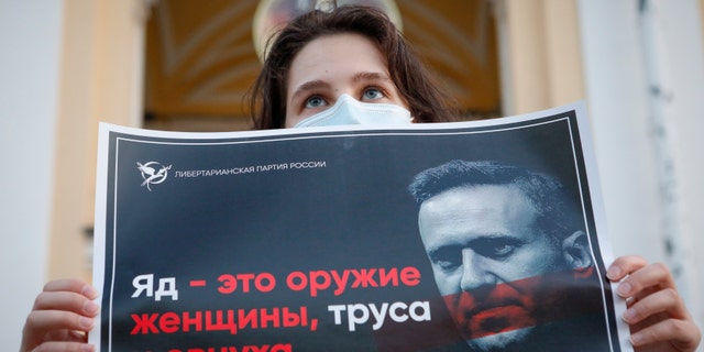 A protester stands holds a poster reads "poison is the weapon of a woman, a coward and a eunuch!" during a picket in support of Russian opposition leader Alexei Navalny in the center of St. Petersburg, Russia, Thursday, Aug. 20, 2020. (AP Photo/Elena Ignatyeva)