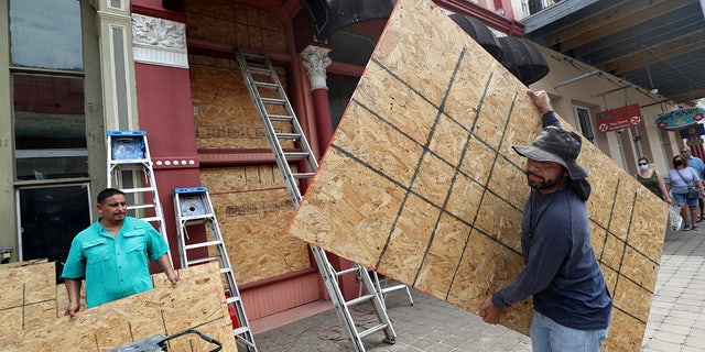 Cesar Reyes, right, carries a sheet of plywood to cut to size as he and Robert Aparicio, left, install window coverings at Strand Brass and Christmas on the Strand, 2115 Strand St., in Galveston on Monday, Aug. 24, 2020. ( Jennifer Reynolds/The Galveston County Daily News via AP)