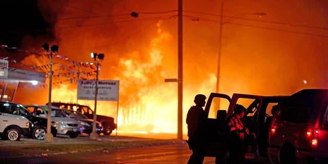 Police trying to secure businesses after protesters set fire to an office in the background late Monday in Kenosha, Wis. (AP Photo/David Goldman)
