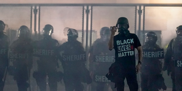 A protester holds up a phone as he stands in front of authorities in Kenosha, Wis on Aug. 25, 2020. (AP Photo/Morry Gash, File)