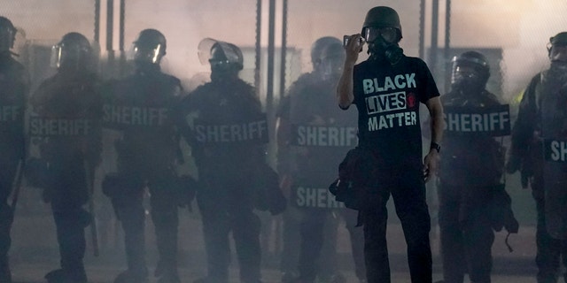 A protester holds up a phone as he stands in front of authorities in Kenosha, Wis. (AP Photo/Morry Gash, File)