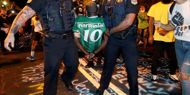 Metropolitan Police carry away a handcuffed protester along a section of 16th Street, Northwest, renamed Black Lives Matter Plaza, Thursday night, Aug. 27, 2020, in Washington, D.C. (AP Photo/Julio Cortez)