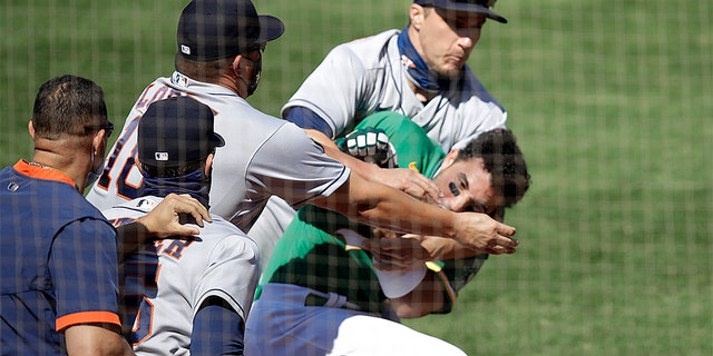 Oakland Athletics' Ramon Laureano is restrained by Houston Astro's Dustin Garneau after Laureano charged the dugout after being hit by a pitch thrown by Humberto Castellanos in the seventh inning of a baseball game Sunday, Aug. 9, 2020, in Oakland, Calif.