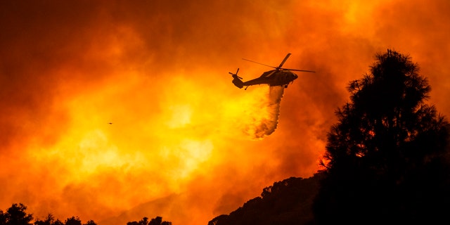 In this Aug. 12, 2020, file photo, a helicopter drops water on the Lake Hughes Fire in Angeles National Forest north of Santa Clarita, Calif.