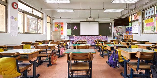 Interior of classroom in elementary school. Row of empty desks are in illuminated room.
