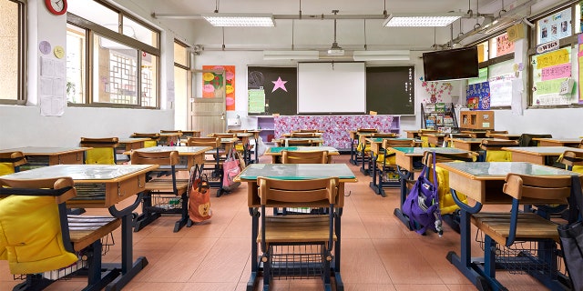 Intérieur de la salle de classe à l'école primaire.  Une rangée de bureaux vides se trouve dans une pièce éclairée.