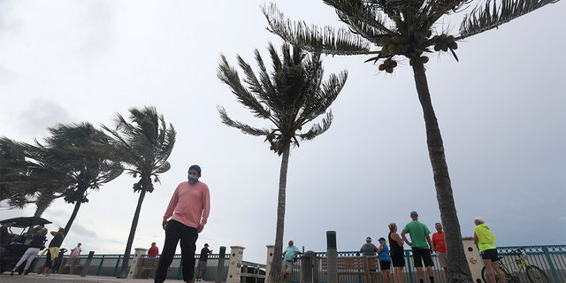 People gather to watch the strong waves on the beach as palm trees sway in the wind on Sunday in Vero Beach, Fla. Isaias weakened from a hurricane to a tropical storm late Saturday afternoon, but was still expected to bring heavy rain and flooding as it barrels toward Florida. (AP Photo/Wilfredo Lee)