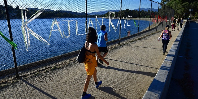 People walk past a chain-link fence surrounding Silver Lake Reservoir in Los Angeles, where an art installation protesting police brutality spells out, in colourful woven fabric, the names of unarmed African Americans who have been killed by police. 