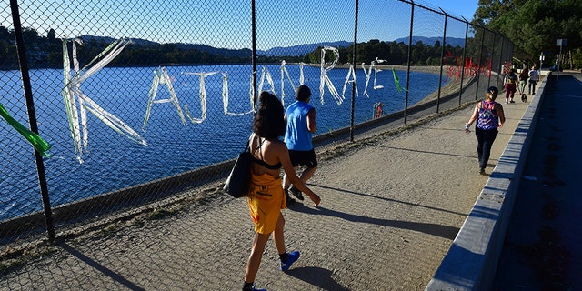 People walk past a chain-link fence surrounding Silver Lake Reservoir in Los Angeles, where an art installation protesting police brutality spells out, in colourful woven fabric, the names of unarmed African Americans who have been killed by police.