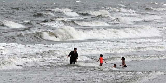 People swim in the ocean as Tropical Storm Isaias approaches in Kure Beach, N.C., Monday, Aug. 3, 2020.