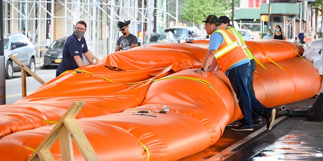 Workers erect temporary flood barriers in the South Street Seaport neighborhood in preparation for potential flooding and a storm surge from Tropical Storm Isaias on August 03, 2020 in New York City. The storm, which is heading up the East Coast packing heavy winds, is expected to dump several inches of rain on the metro area starting late this evening and into tomorrow. The interlocking tubes, called Tiger Dams, are installed in areas that were heavily damaged from flooding during Hurricane Sandy.
