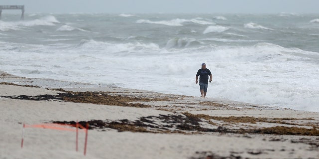 A beach goer walks along the shore as waves churned up by Tropical Storm Isaias crash near Jaycee Beach Park, Sunday, Aug. 2, 2020, in Vero Beach, Fla.