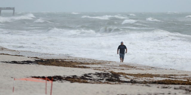 A beach goer walks along the shore as waves churned up by Tropical Storm Isaias crash near Jaycee Beach Park, Sunday, Aug. 2, 2020, in Vero Beach, Fla.