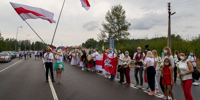 Supporters of Belarus opposition from Lithuania hold and wave historical Belarusian flags during the "Freedom Way", a human chain of about 50,000 strong from Vilnius to the Belarusian border, near Medininkai, Lithuanian-Belarusian border crossing east of Vilnius, Lithuania, Sunday, Aug. 23, 2020. In Aug. 23, 1989, around 2 million Lithuanians, Latvians, and Estonians joined forces in a living 600 km (375 mile) long human chain Baltic Way, thus demonstrating their desire to be free. Now, Lithuania is expressing solidarity with the people of Belarus, who are fighting for freedom today. (AP Photo/Mindaugas Kulbis)