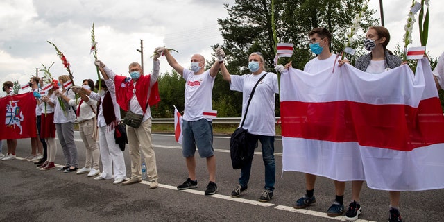 People hold hands, historical white-red-white flags of Belarus and flowers as they participate in a "Freedom Way", a human chain of about 50,000 strong from Vilnius to the Belarusian border, during a protest near Medininkai, Lithuanian-Belarusian border crossing east of Vilnius, Lithuania, Sunday, Aug. 23, 2020. In Aug. 23, 1989, around 2 million Lithuanians, Latvians, and Estonians joined forces in a living 600 km (375 mile) long human chain Baltic Way, thus demonstrating their desire to be free. Now, Lithuania is expressing solidarity with the people of Belarus, who are fighting for freedom today. (AP Photo/Mindaugas Kulbis)